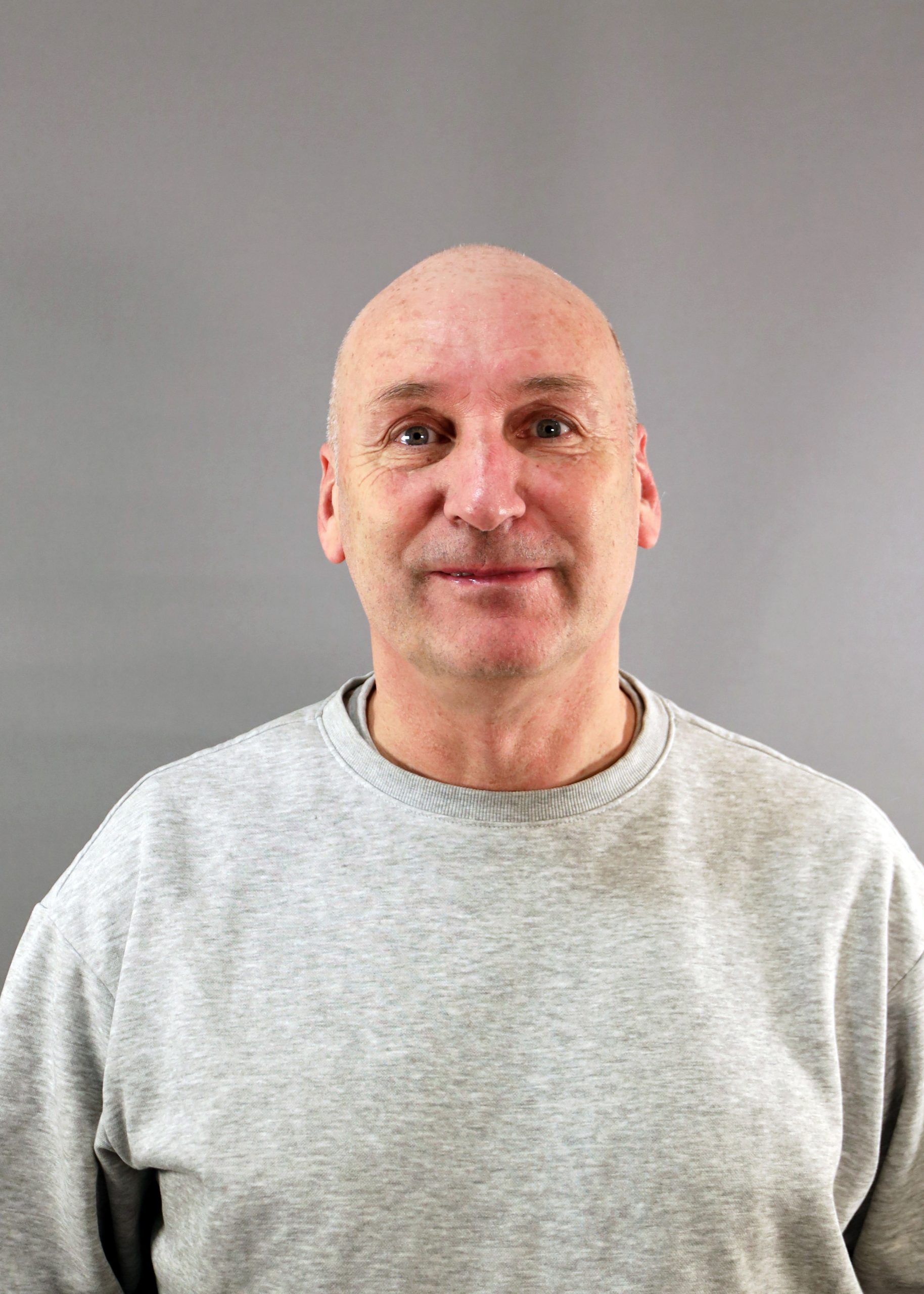 En leende skallig man i ljusgrå sweatshirt står mot en grå bakgrund.