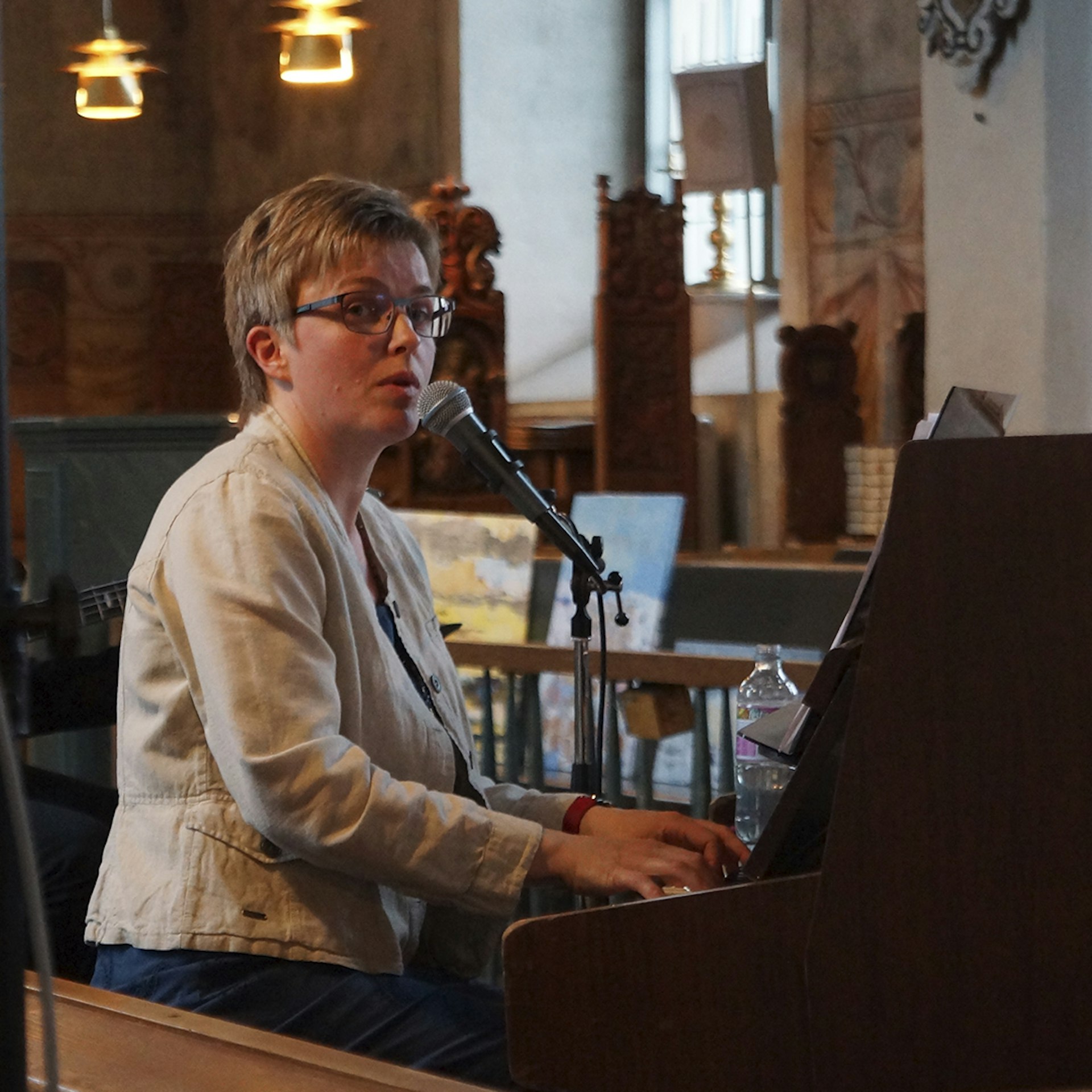 En kvinna spelar piano och sjunger i en mikrofon i ett varmt upplyst rum.