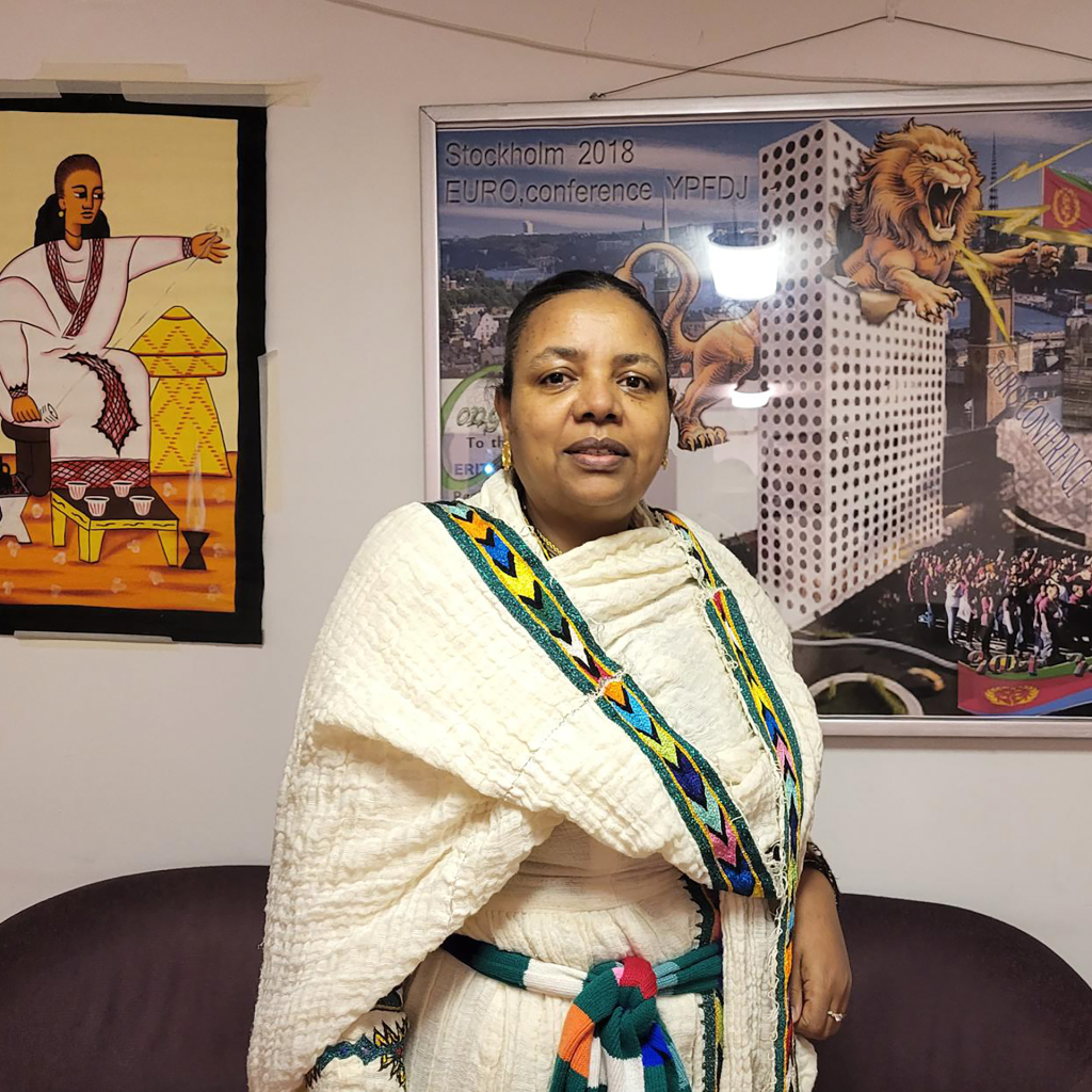 En kvinna i traditionell etiopisk klädsel står inomhus med konst och en affisch från konferensen Bildas folkbildningspris på väggen bakom sig.