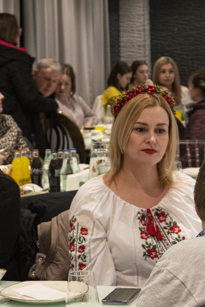 Kvinna i broderad blus med blommigt pannband sitter vid ett bord på en välbesökt restaurang.