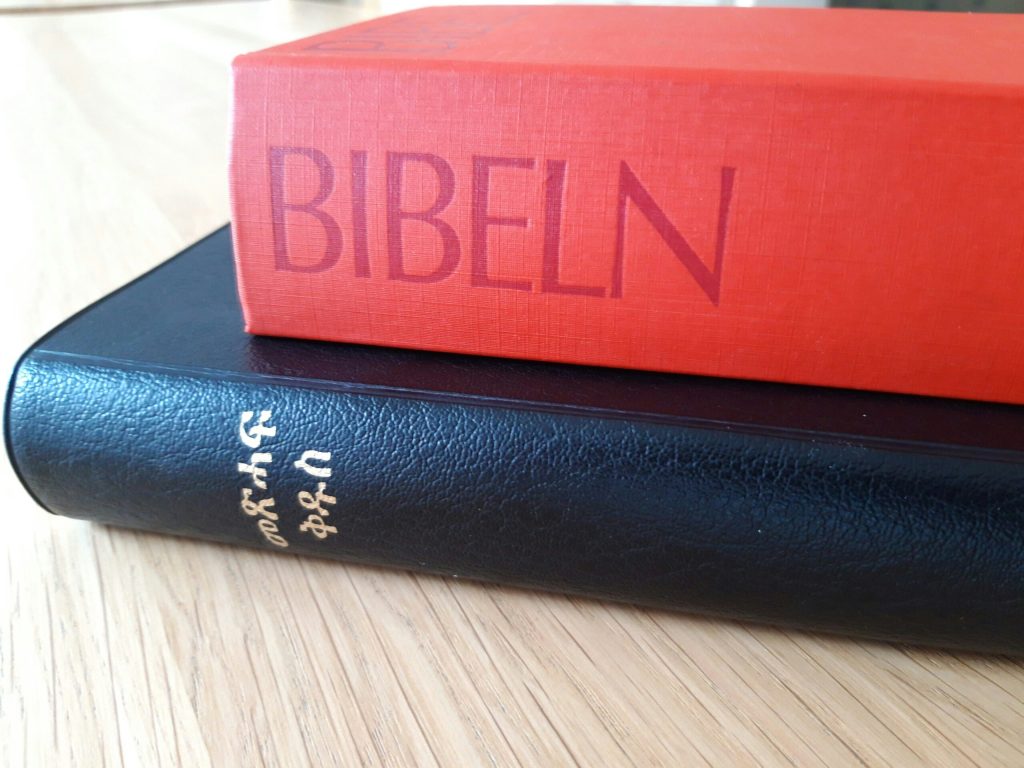 En röd svensk bibel och en svart amharisk bibel staplade på en ljus träyta.
