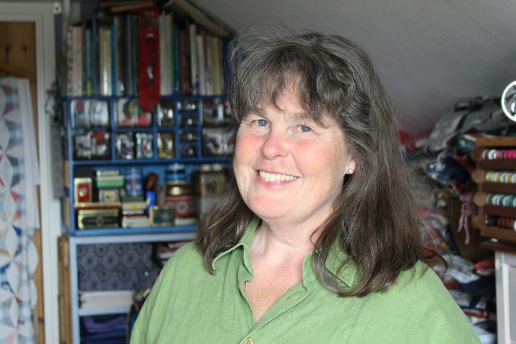 Kvinna i grön skjorta och brunt hår tittar leende in i kameran.