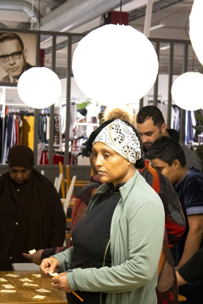 En kvinna med huvudduk står och håller i post-it-lappar i en väl upplyst butik med andra människor omkring sig.