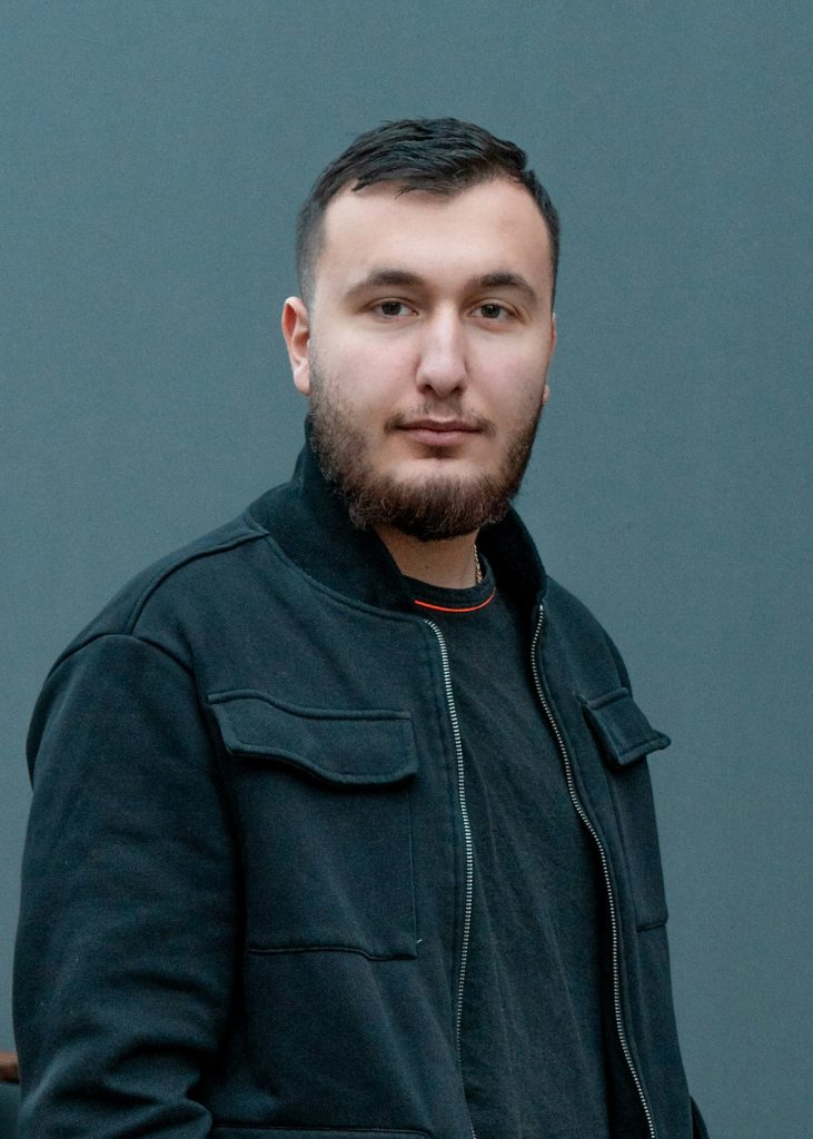 Man med kort hår och skägg iklädd svart jacka står framför en grå bakgrund och representerar Syrisk-ortodoxa kyrkans ungdomsförbund.