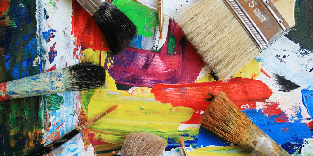 Olika penslar vilar på en färgstark, abstrakt målad duk med djärva streck i rött, grönt, gult och blått.