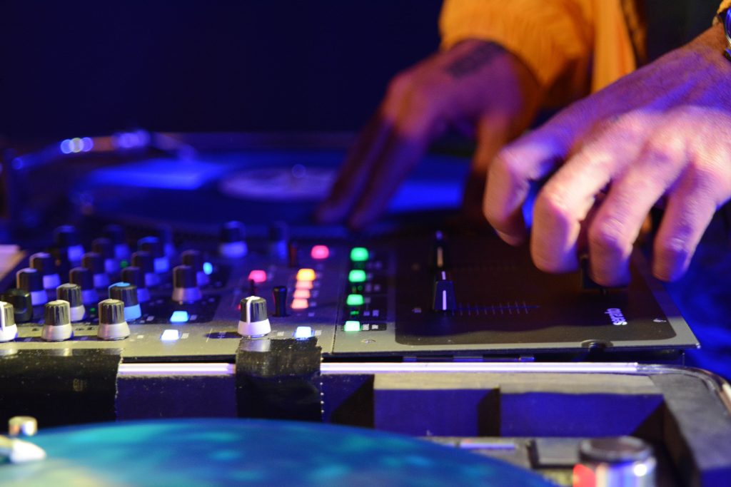 Närbild på en DJ:s händer som mixar musik på en ljudplatta med färgglada lampor och skivspelare.