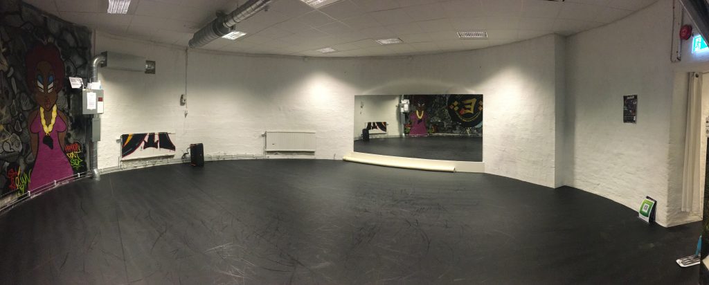Rymlig dansstudio med svart golv, vita väggar, graffitikonst och stor väggspegel.