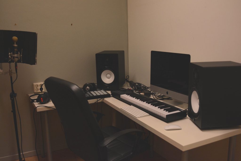 En musikstudio i hemmet med dator, högtalare, keyboard, hörlurar och en mikrofon på stativ.
