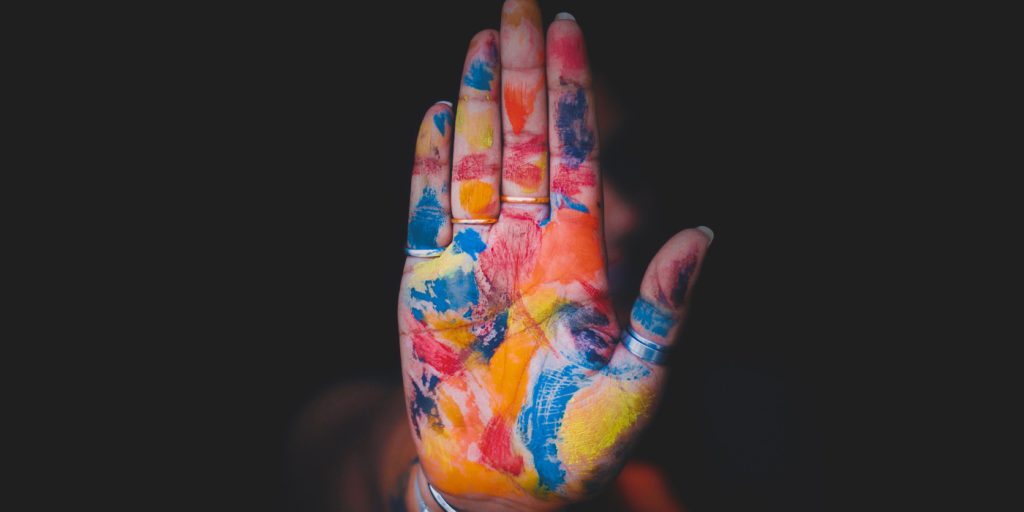 En hand täckt av färgglad färg hålls upp mot en mörk bakgrund.