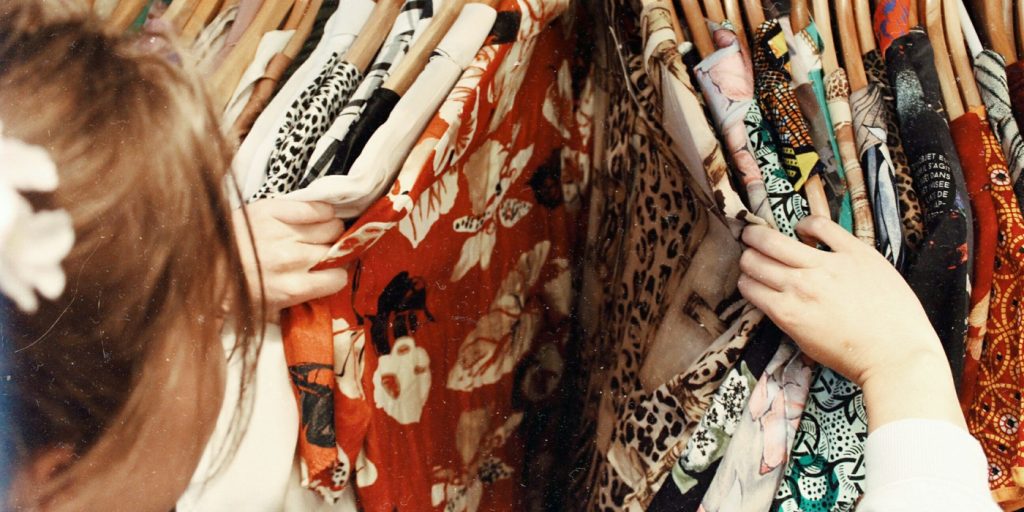 En person bläddrar bland färgglatt mönstrade kläder på galgar i ett klädställ.