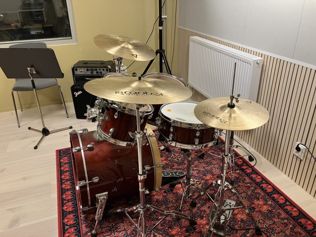 Ett trumset med cymbaler och notställ i ett musikrum på en mönstrad matta.