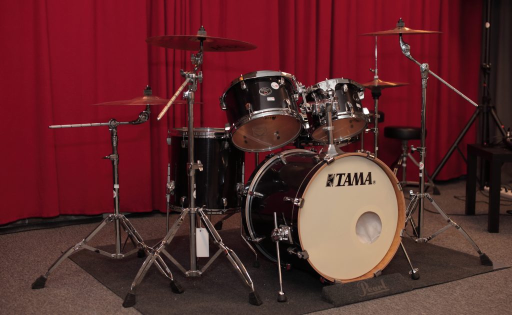 Ett svart trumset av märket Tama visas på en scen framför röda gardiner.