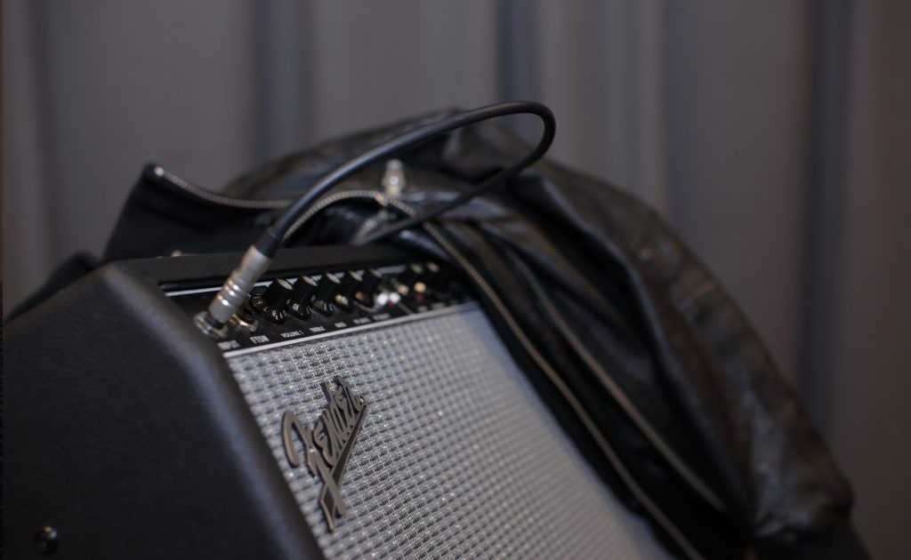 Närbild på en Fender gitarrförstärkare med en kabel inkopplad och en svart läderjacka draperad över den.