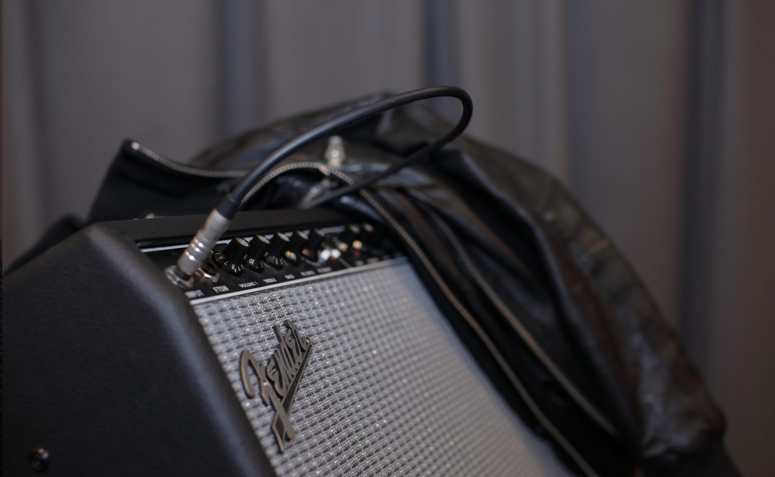Närbild på en Fender gitarrförstärkare med en kabel inkopplad och en svart läderjacka draperad över den.