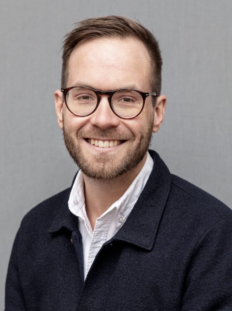 bild på leende man fotograferad mot grå bakgrund