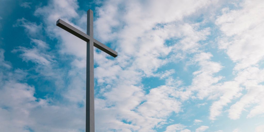 Ett stort vitt kors står mot en ljusblå himmel med spridda moln.
