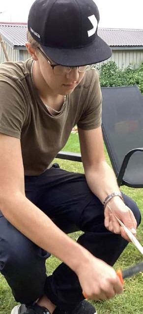 en ung man som sitter på en bänk och täljer.