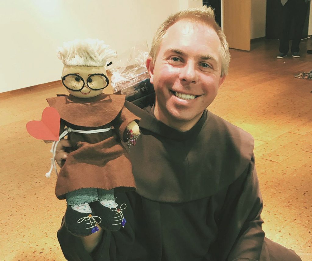 En person i en brun mantel ler medan han håller en docka i matchande klädsel.