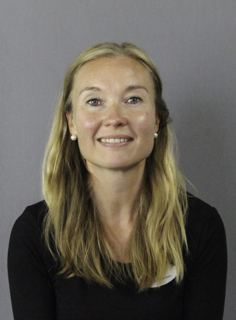 Carina i en svart skjorta ler mot kameran.