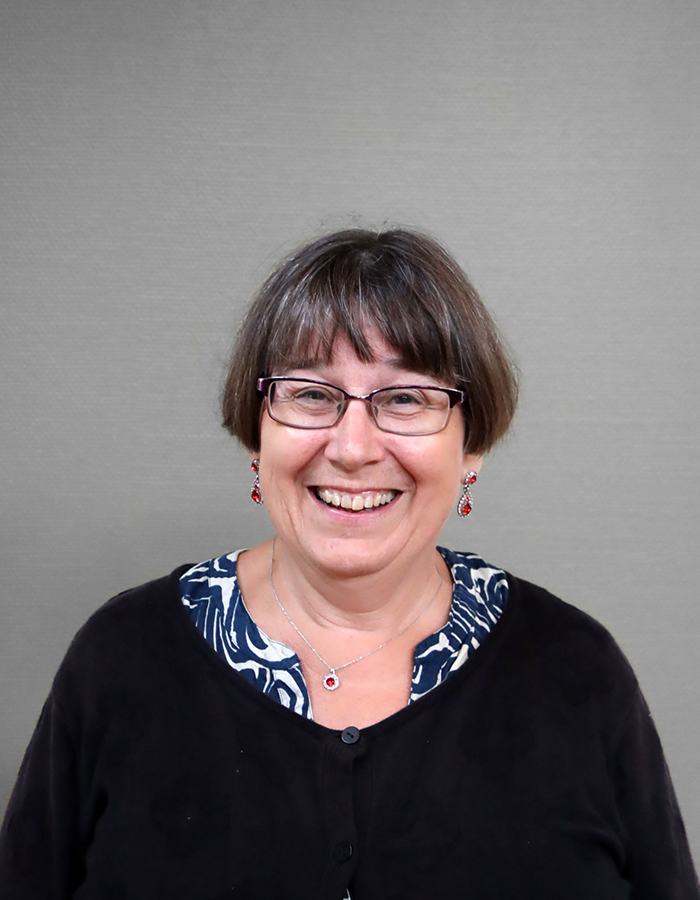 Kvinna med kort hår och örhängen ler stort in i kameran.