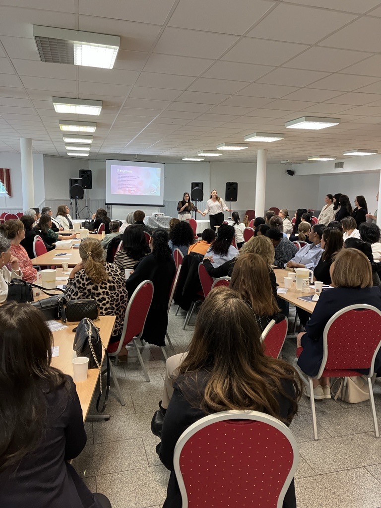 I ett konferensrum sitter en stor grupp människor vid bord som vetter mot högtalare och en presentationsskärm.