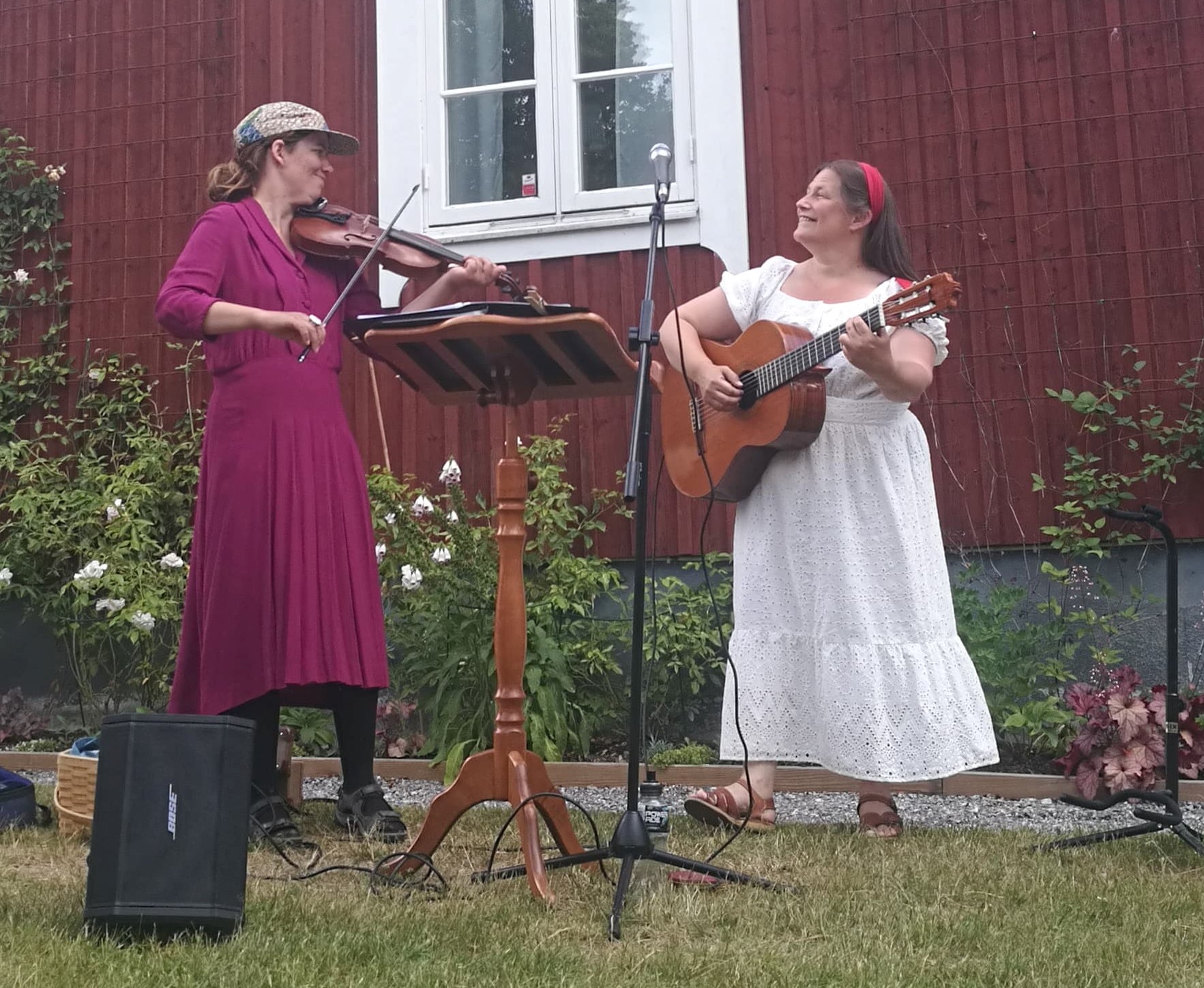 Två musiker står framför ett rött trähus och spelar.