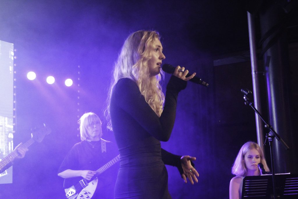 En kvinna i en svart klänning sjunger i en mikrofon.