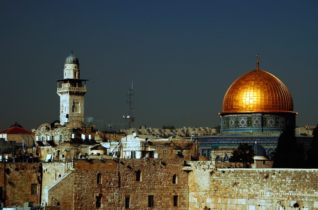 Klippdomen och minareten höjer sig över gamla stenbyggnader i Jerusalem under en klar himmel.