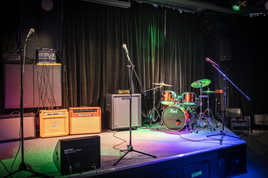 Tom musikscen med mikrofoner, förstärkare och ett trumset under färgglada scenljus.