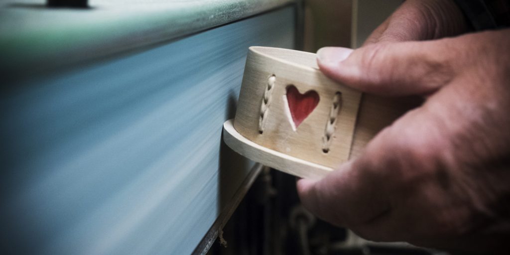Närbild av händer som slipar ett träföremål med ett utskuret rött hjärta på en slipmaskin.