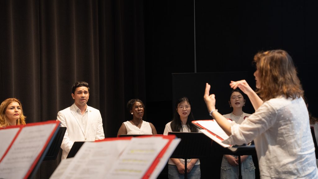 En kör sjunger medan en dirigent leder dem, med noter synliga i förgrunden.