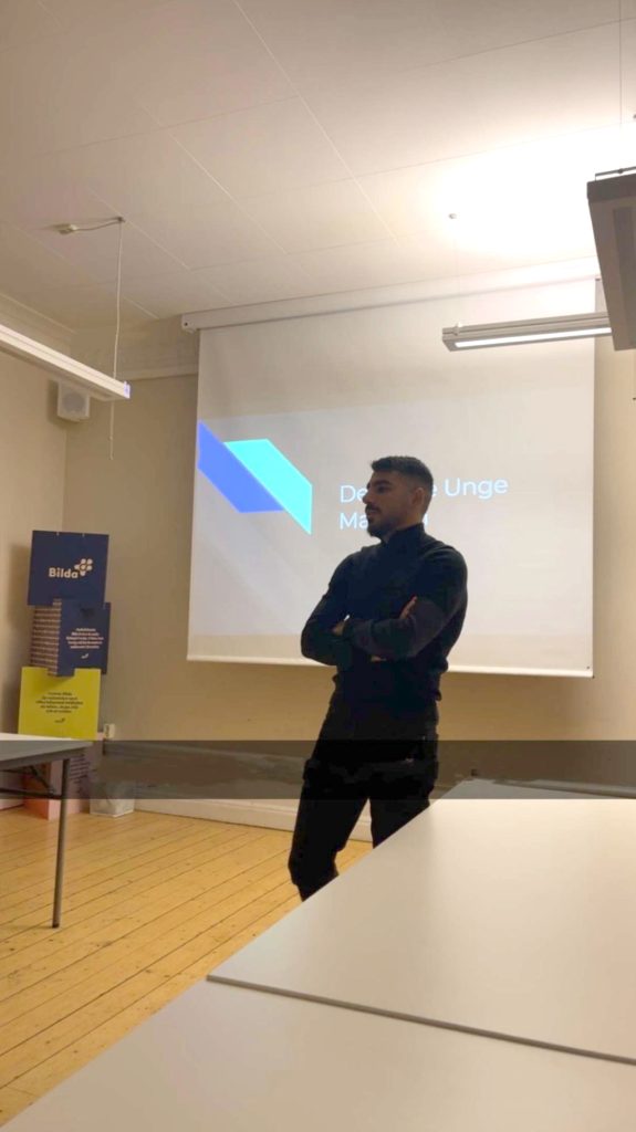 En man står framför en projektorskärm och håller en presentation i ett klassrum.