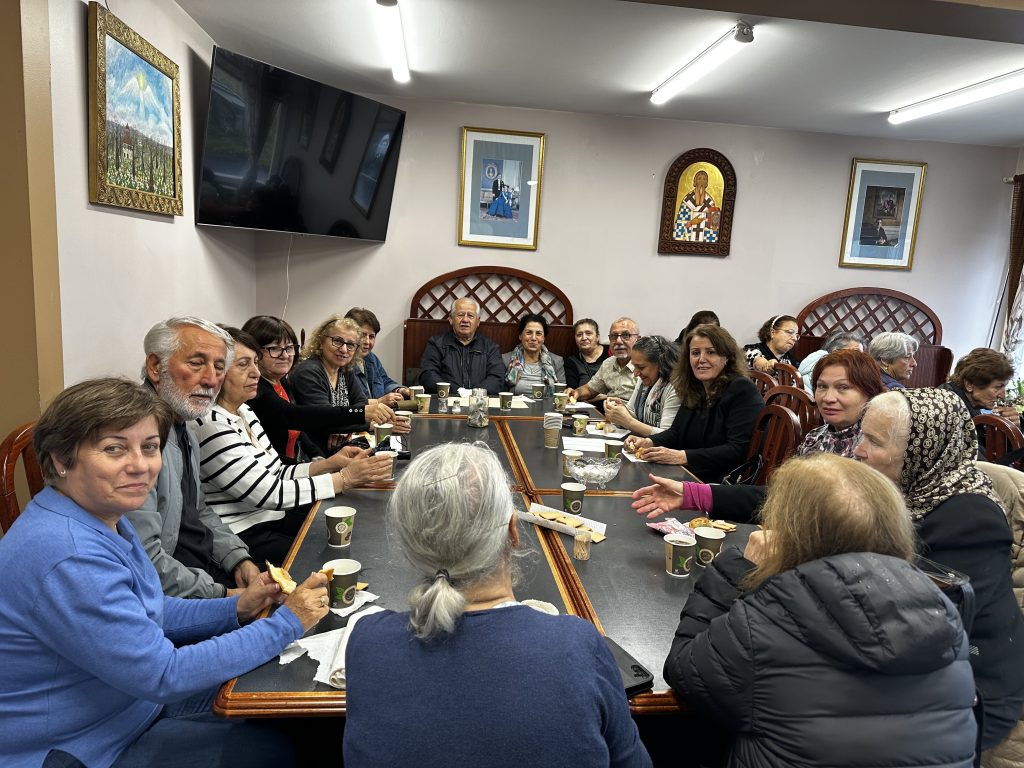 En grupp vuxna sitter runt borden och ler och småpratar medan de njuter av drinkar och snacks i ett mysigt rum.