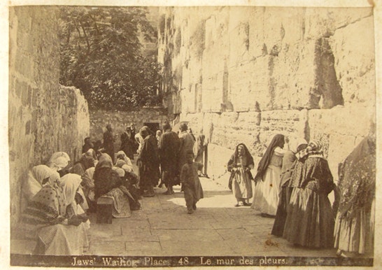 En grupp människor samlas och ber vid Västra muren i Jerusalem på ett gammalt sepiatonat fotografi.