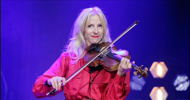 En kvinna i röd blus spelar violin på scenen i lila belysning.