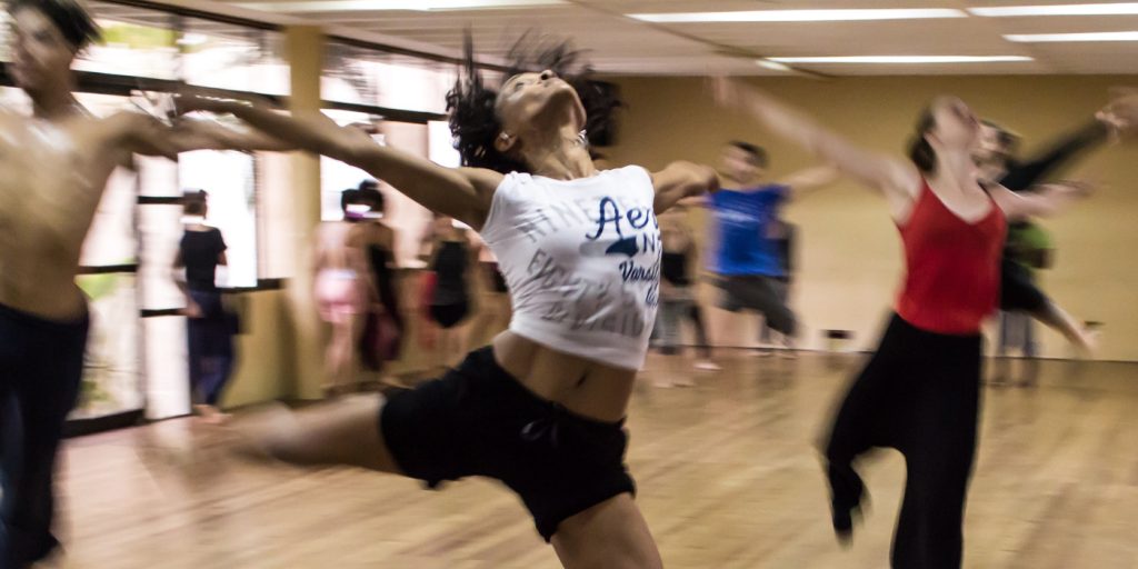 Dansare i rörelse i en studio, med en person som hoppar energiskt i förgrunden.