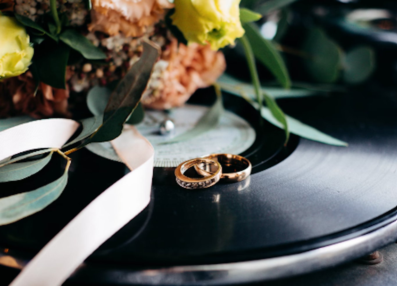 Vigselringar på en vinylskiva bredvid en blombukett och ett vitt band.