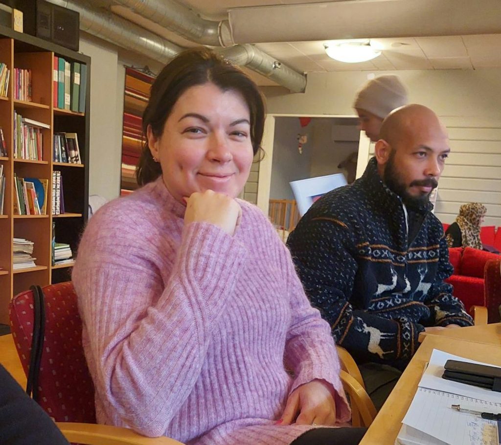 Leende kvinna med mörkt hår och ljusrosa tröja ler in i kameran.