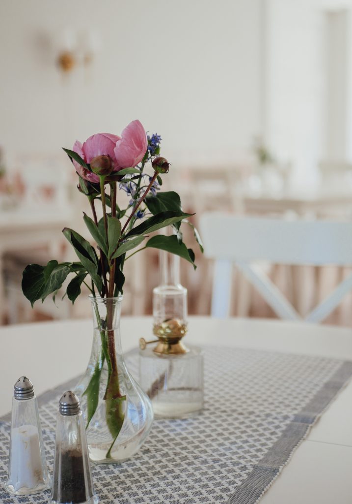 En liten vas med rosa och lila blommor står på ett bord med salt- och pepparkar samt en glaslampa.