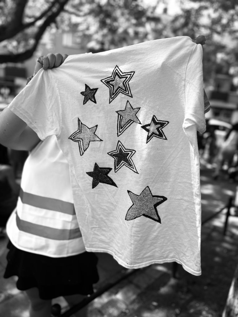 Person med vit skjorta dekorerad med nio svarta stjärnmönster, utomhus i dagsljus.