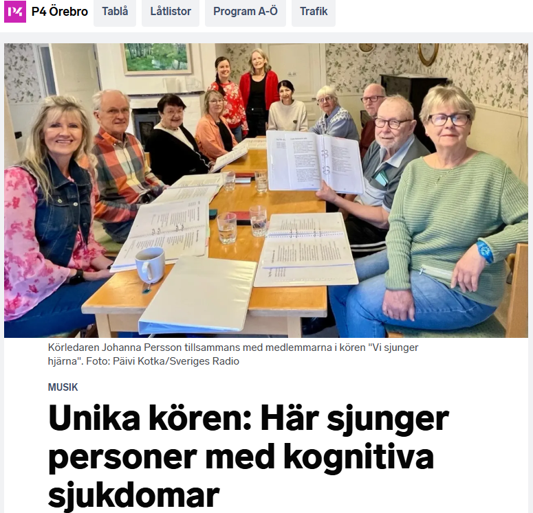 En kör av personer med kognitiva sjukdomar sitter runt ett bord, ler och håller i notblad - njuter av musikglädje tillsammans med Vi sjunger hjärna.