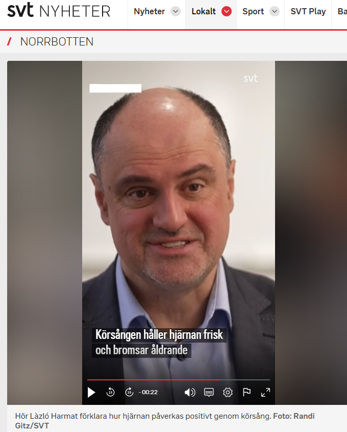 En kostymklädd man talar i en intervju; svensk textning visas på skärmen med frasen "Vi sjunger hjärna.