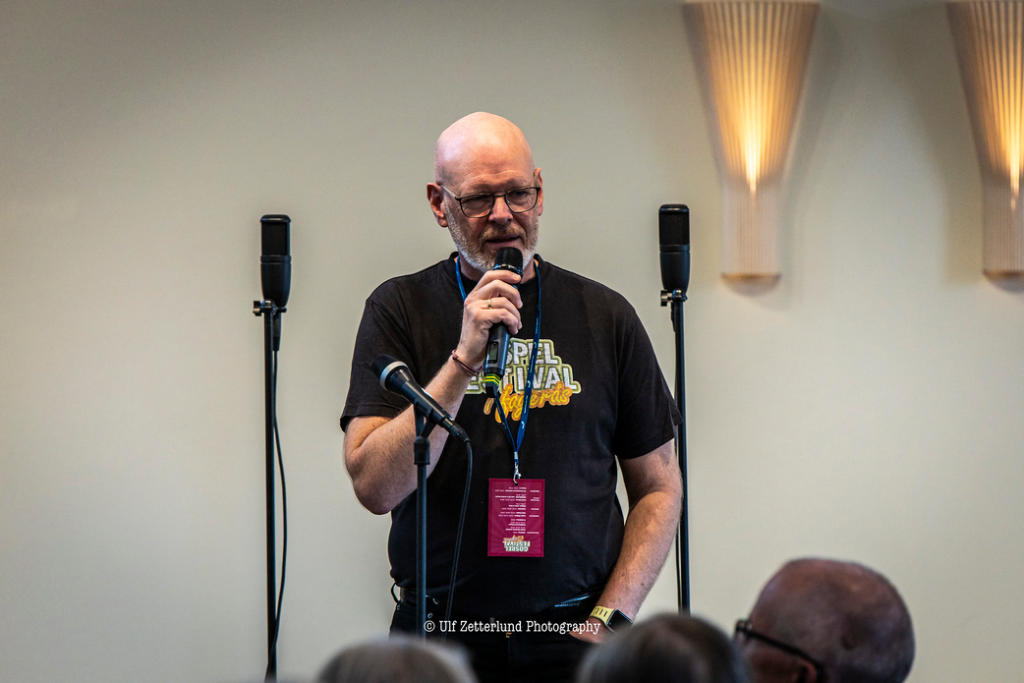 En man står på en scen och pratar i en mikrofon.