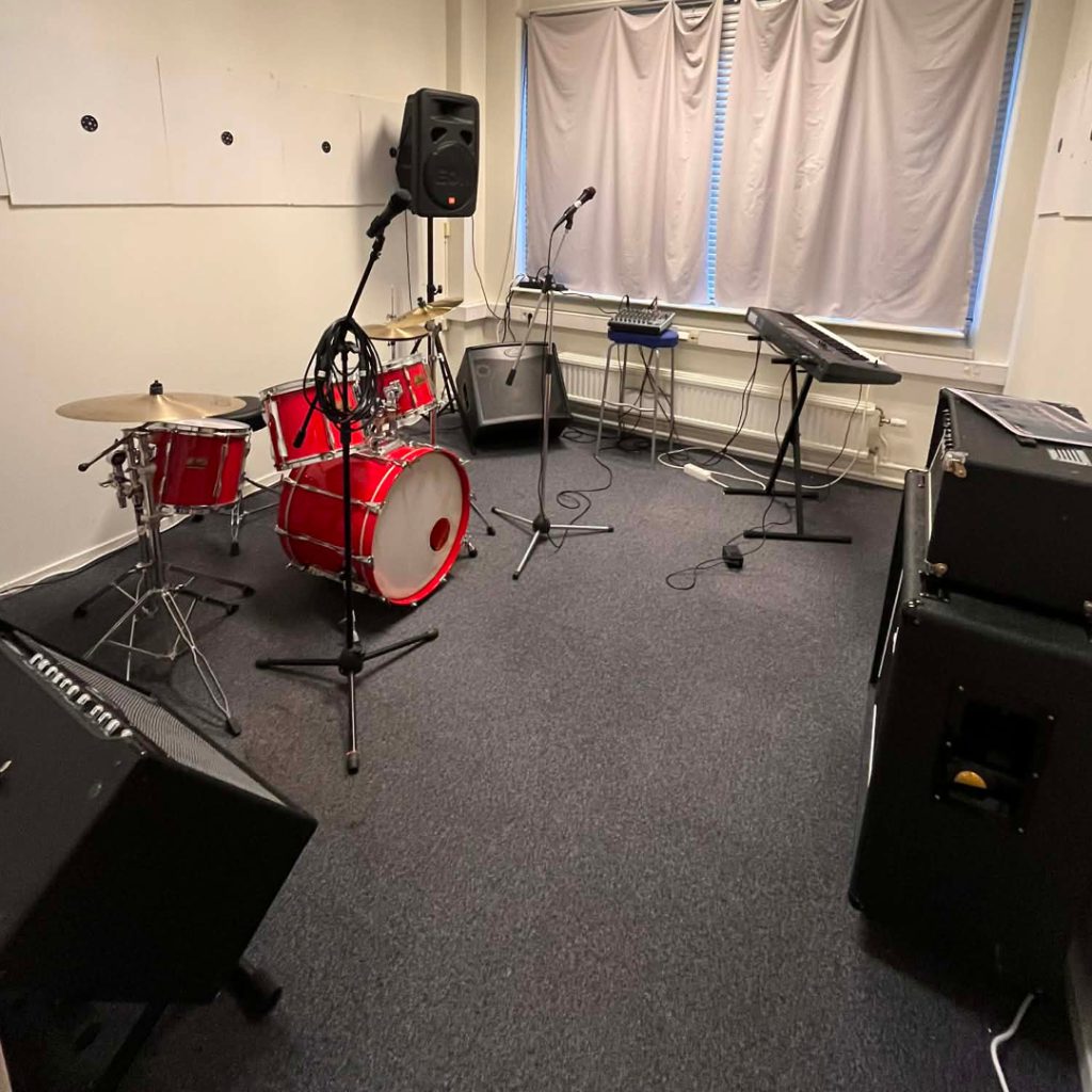 Ett musikrepetitionsrum med ett rött trumset, keyboards, mikrofoner och förstärkare.