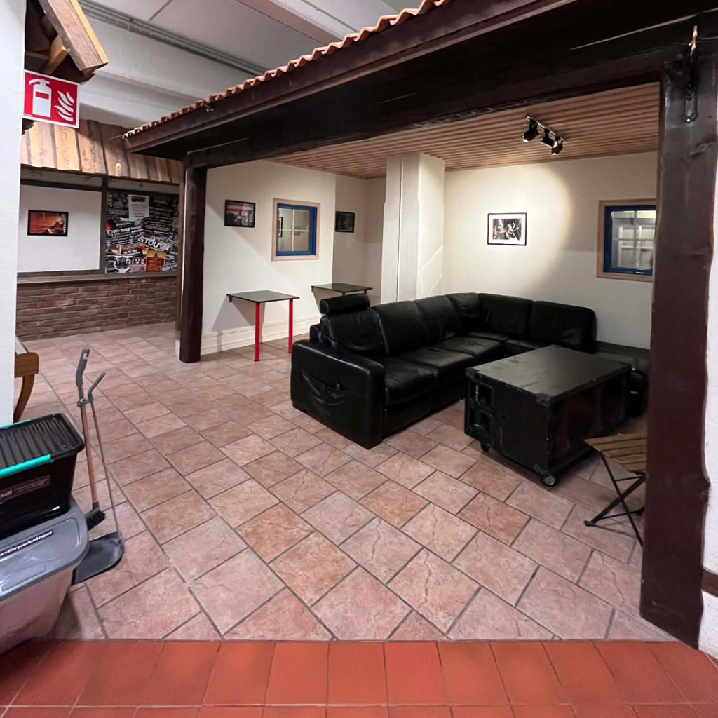 Ett vardagsrum med en svart soffa, soffbord, klinkergolv, inramade foton och rengöringsmedel i hörnet.