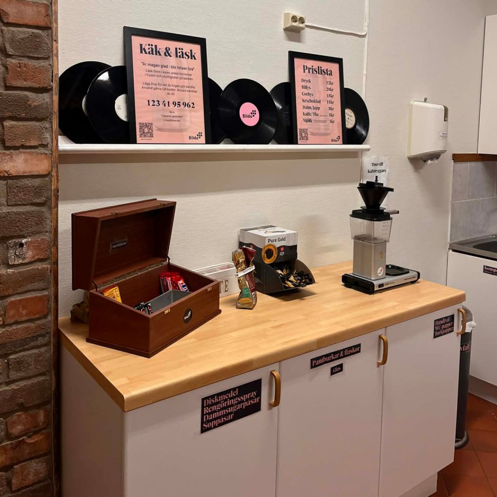 Ett pentry med en snackbox, kaffekvarn, vinylskivor och prislistor på väggen.