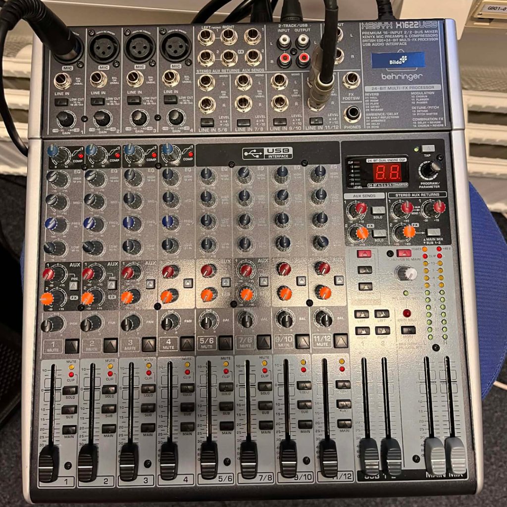 En Behringer Xenyx ljudmixer med flera rattar, reglage och ingångskablar som är inkopplade längst upp.