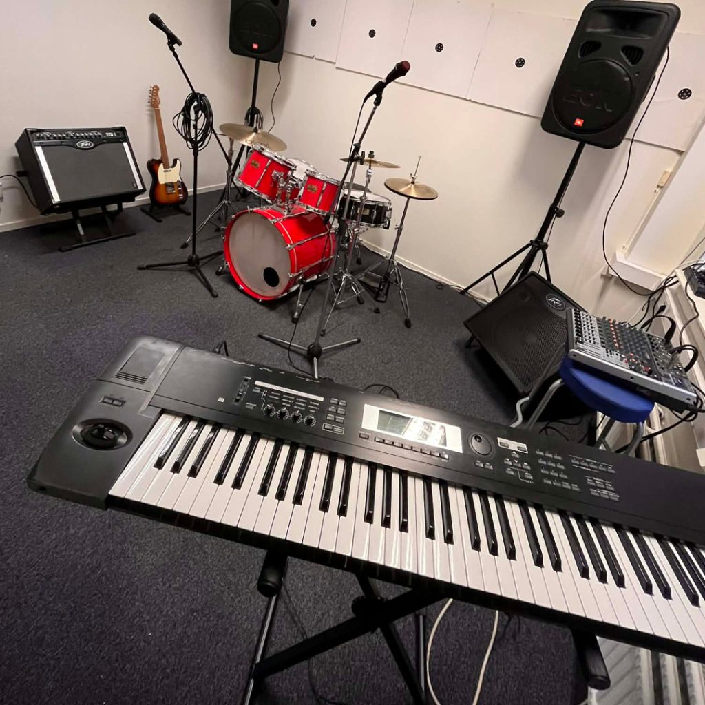 Musikstudio med keyboard, rött trumset, mikrofoner, högtalare, gitarr och ljudmixer.
