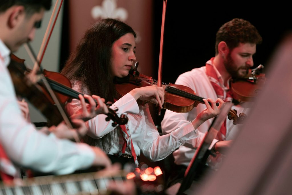 En grupp musiker som spelar violiner i ett liveframträdande, fokuserade och klädda i vita skjortor.