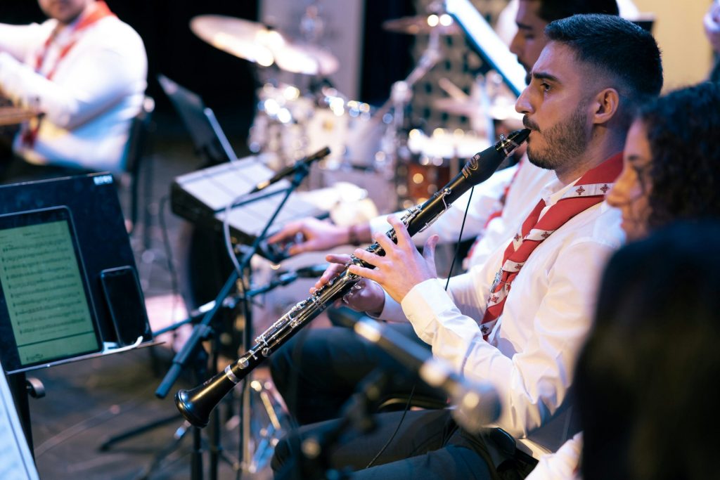 En musiker i vit skjorta spelar klarinett i en orkester under ett liveframträdande.